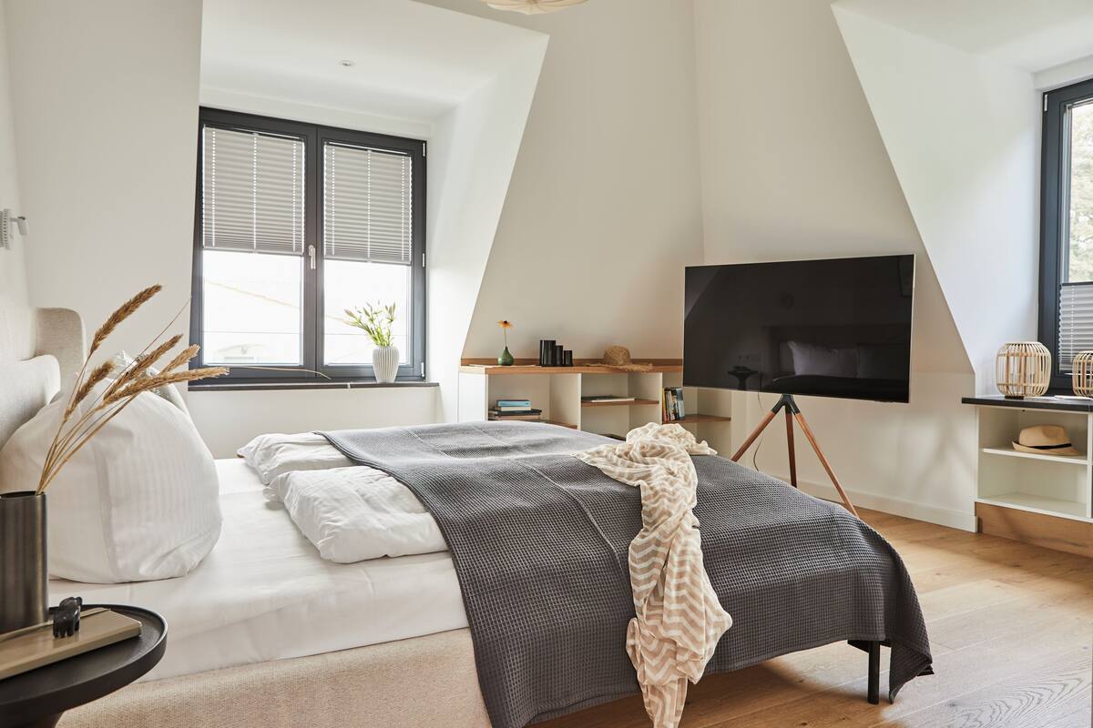 Een moderne slaapkamer met een bed, een flatscreen-tv en een groot raam met zonwering.