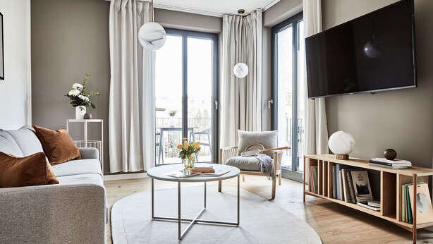 A modern living room with a sofa, coffee table, and bookshelf, featuring a large window and a flat-screen TV. - Villa Baltique Sellin (Sellin)