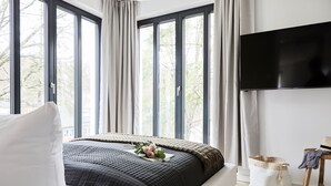 A bedroom with a large bed, a flat-screen TV, and a view of trees through the windows. - Villa Baltique Sellin (Sellin)
