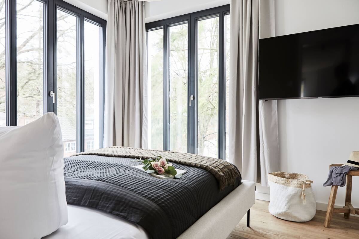 Een slaapkamer met een groot bed, een flatscreen-tv en uitzicht op bomen door de ramen.