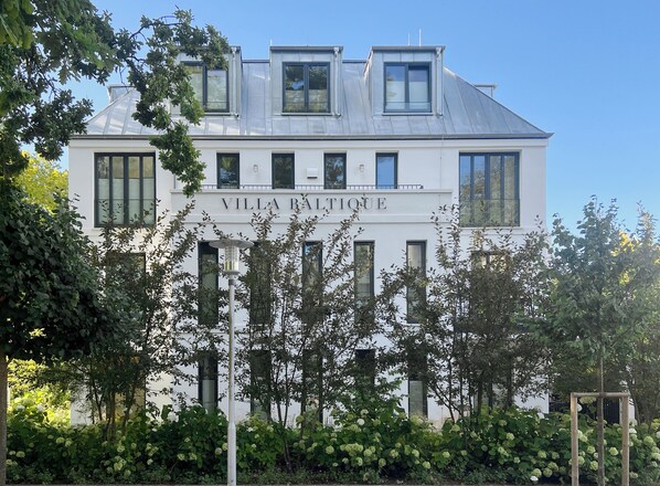 A white building with the name "Villa Baltiqué" on the facade, featuring multiple windows and a sloped roof with skylights. - Villa Baltique Sellin (Sellin)