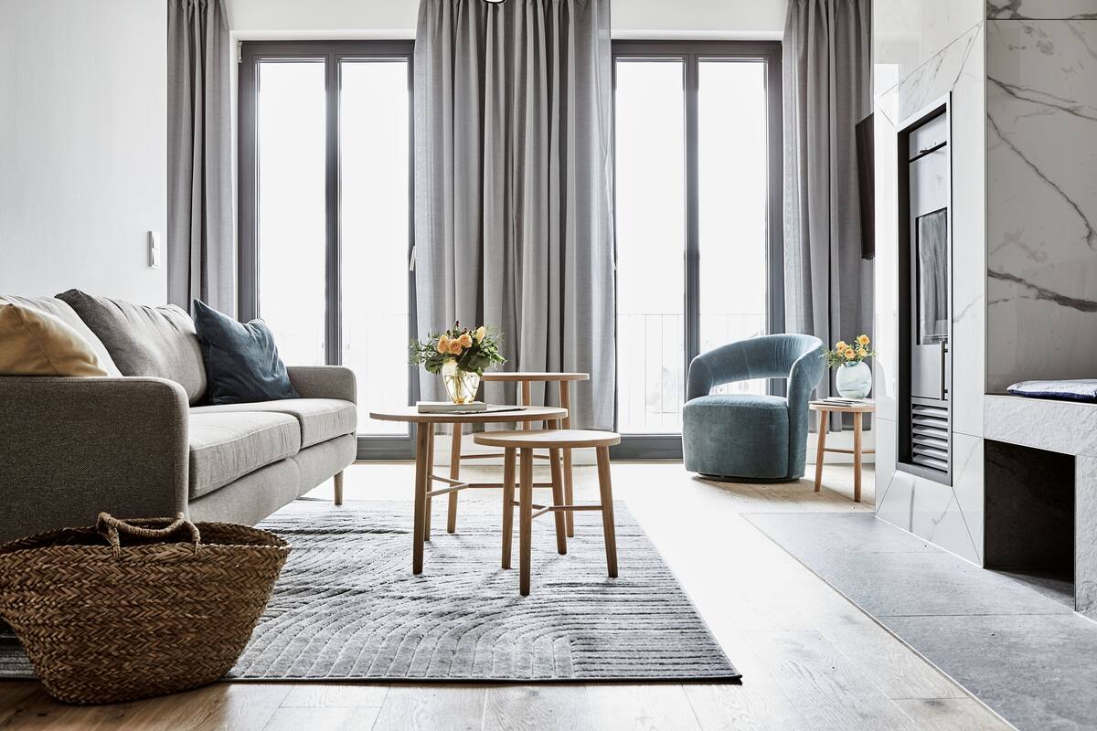 Een moderne woonkamer met een grijze bank, een blauwe fauteuil, een klein rond tafeltje met stoelen en een open haard.