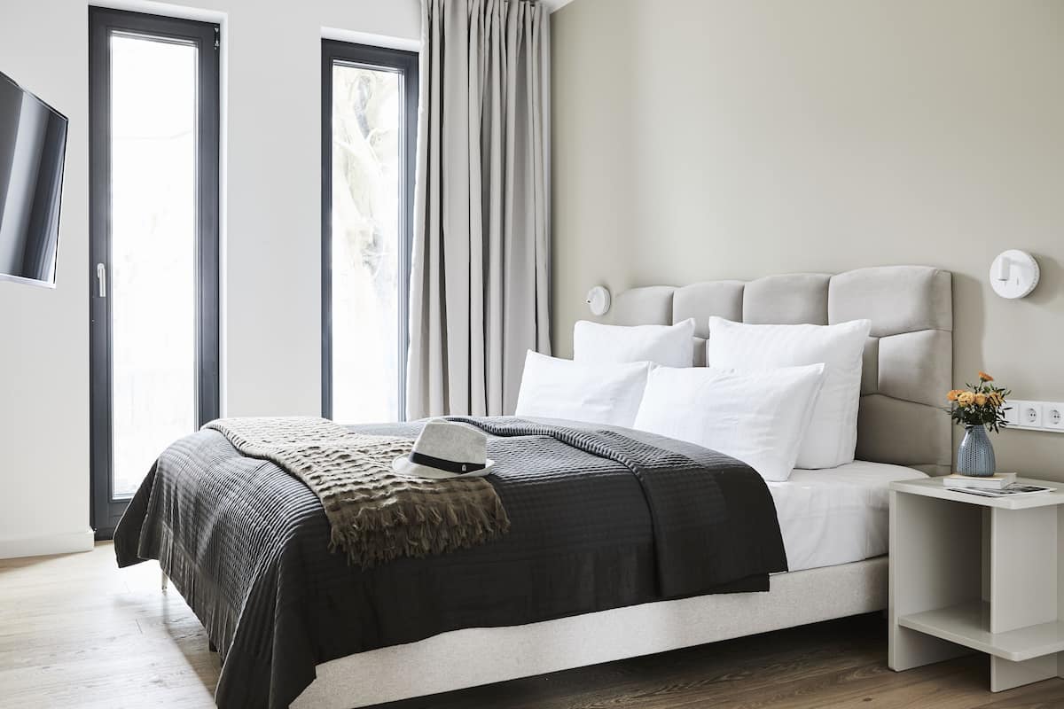 Een moderne slaapkamer met een groot bed, een nachtkastje, een aan de muur bevestigde televisie en een raam met gordijnen.
