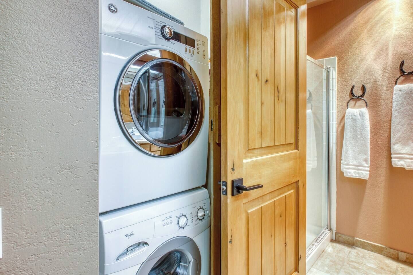 A laundry room with a front-loading washer and dryer, a wooden door, and a towel rack with towels.