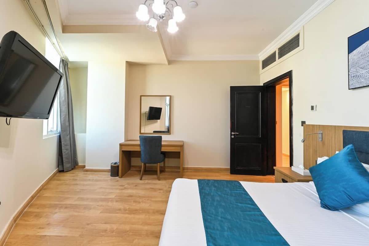 Ett hotellrum med en säng, ett skrivbord, en stol, en tv och en dörr.