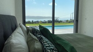 A bedroom with a large window overlooking a swimming pool and a view of the sea.
