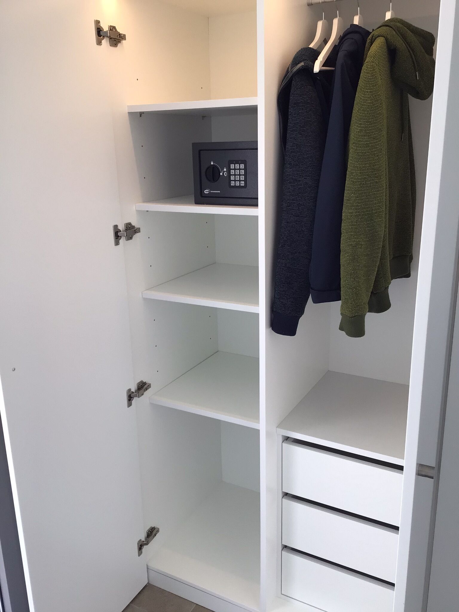 Un placard blanc doté d’un cadenas à combinaison, de plusieurs étagères et d’un espace pour suspendre les vêtements.