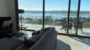 A modern living room with a large sliding glass door leading to a balcony with a view of a coastal landscape.