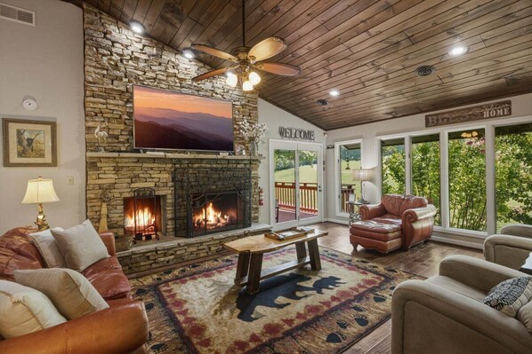 A cozy living room with a stone fireplace, leather sofas, a coffee table, and a large TV.