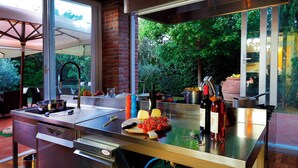 Una cuina moderna amb taulell d'acer inoxidable, forn integrat i finestra amb vista a un jardí.