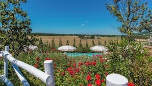 Un jardí amb flors vermelles, una piscina i vistes a camps i cases.