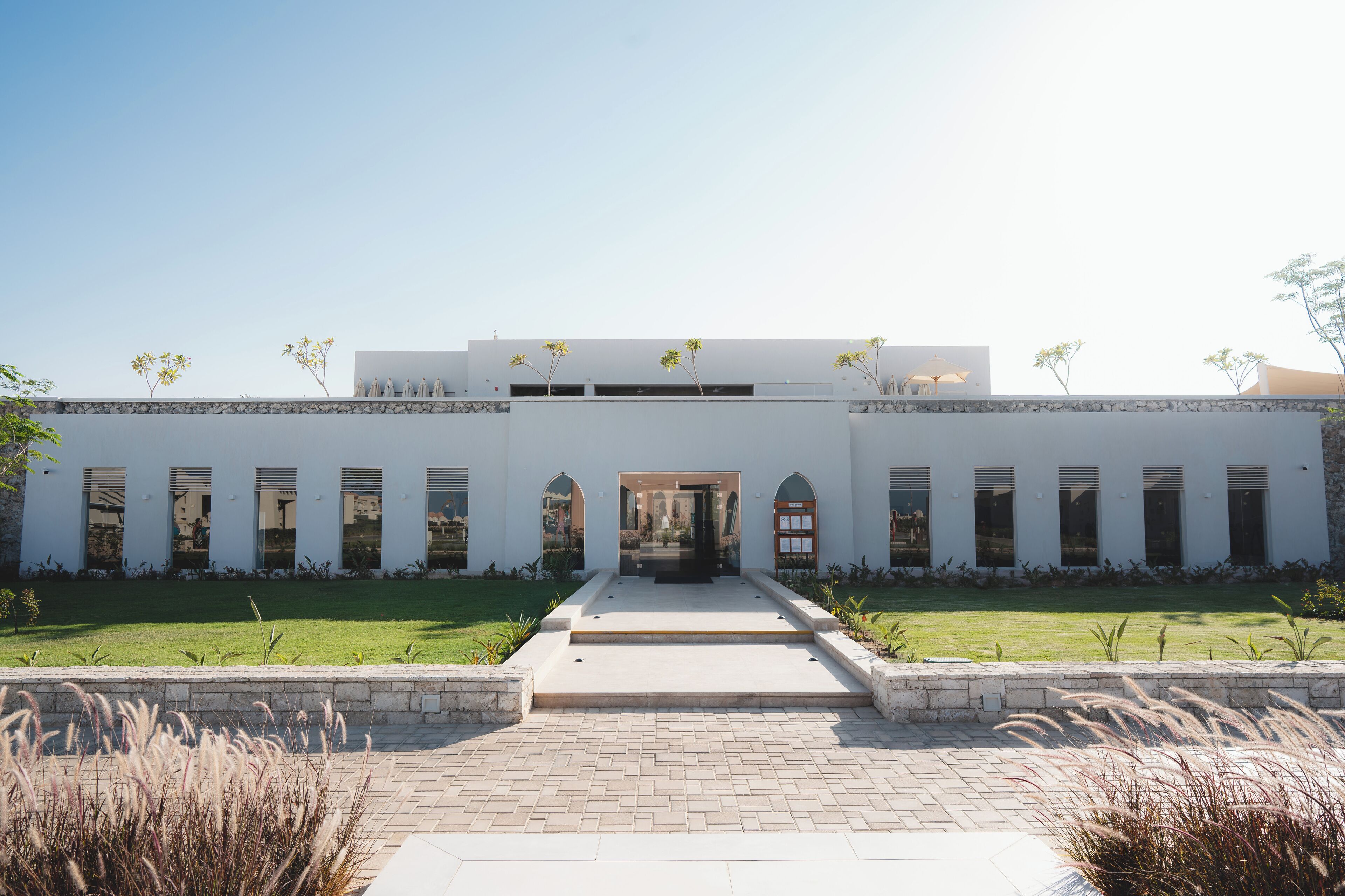 A modern building with a central entrance, symmetrical windows, and a paved pathway leading to the entrance.