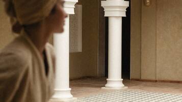 A person in a robe walking through a courtyard with a pool and tiled flooring.