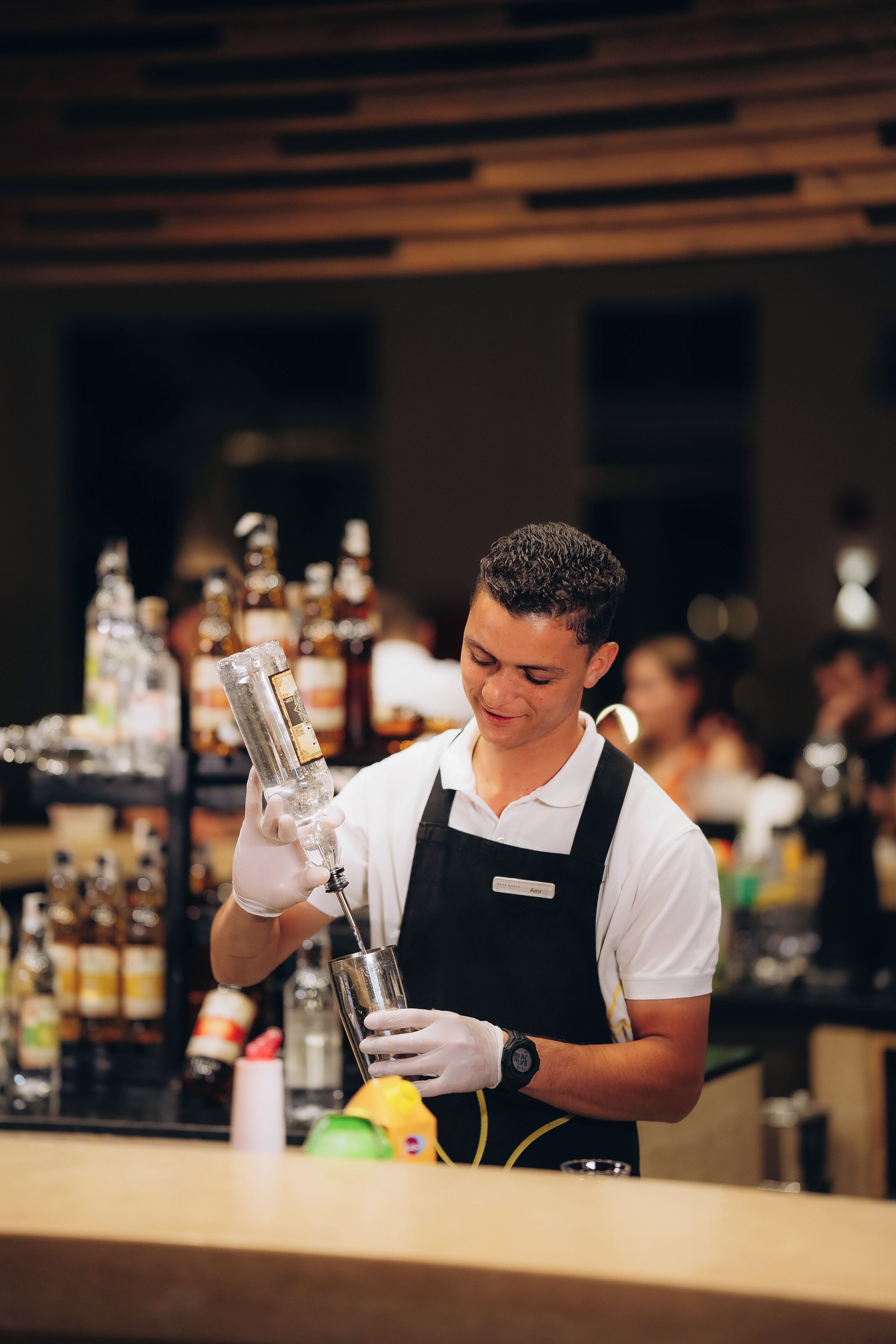 A bartender preparing a drink behind a bar with various bottles and glasses.