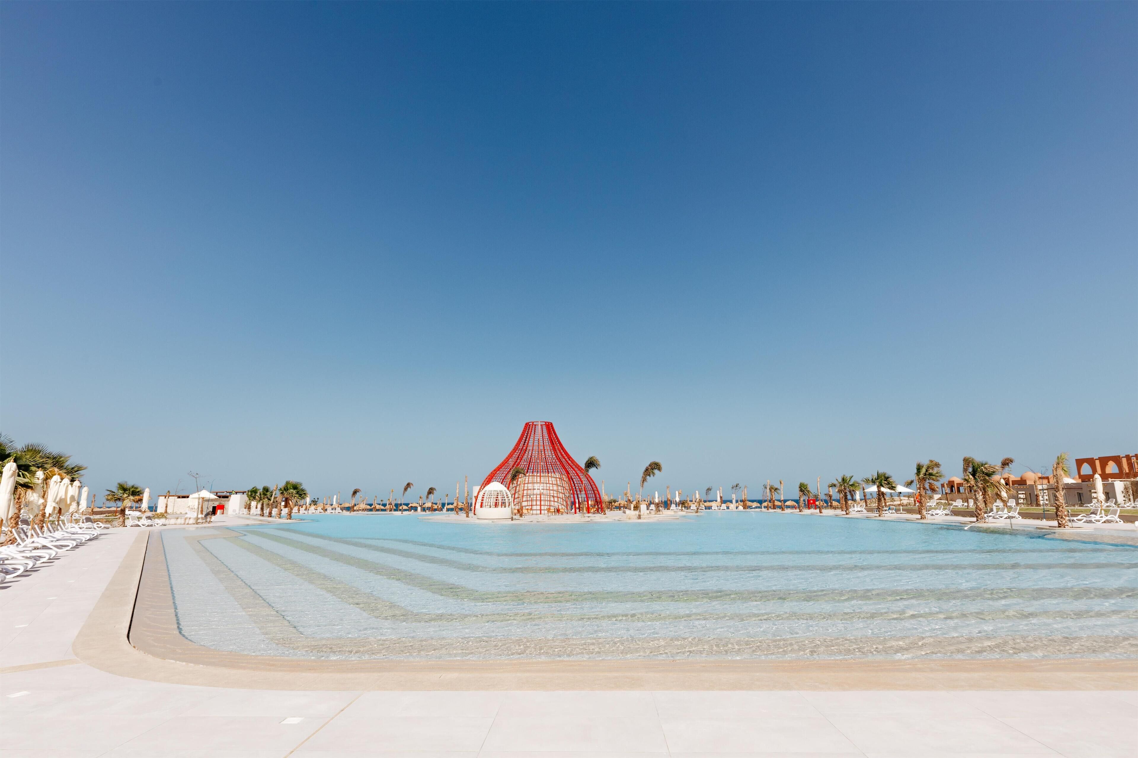 Un complexe hôtelier de bord de mer doté d’une grande piscine, de chaises longues et de palmiers.