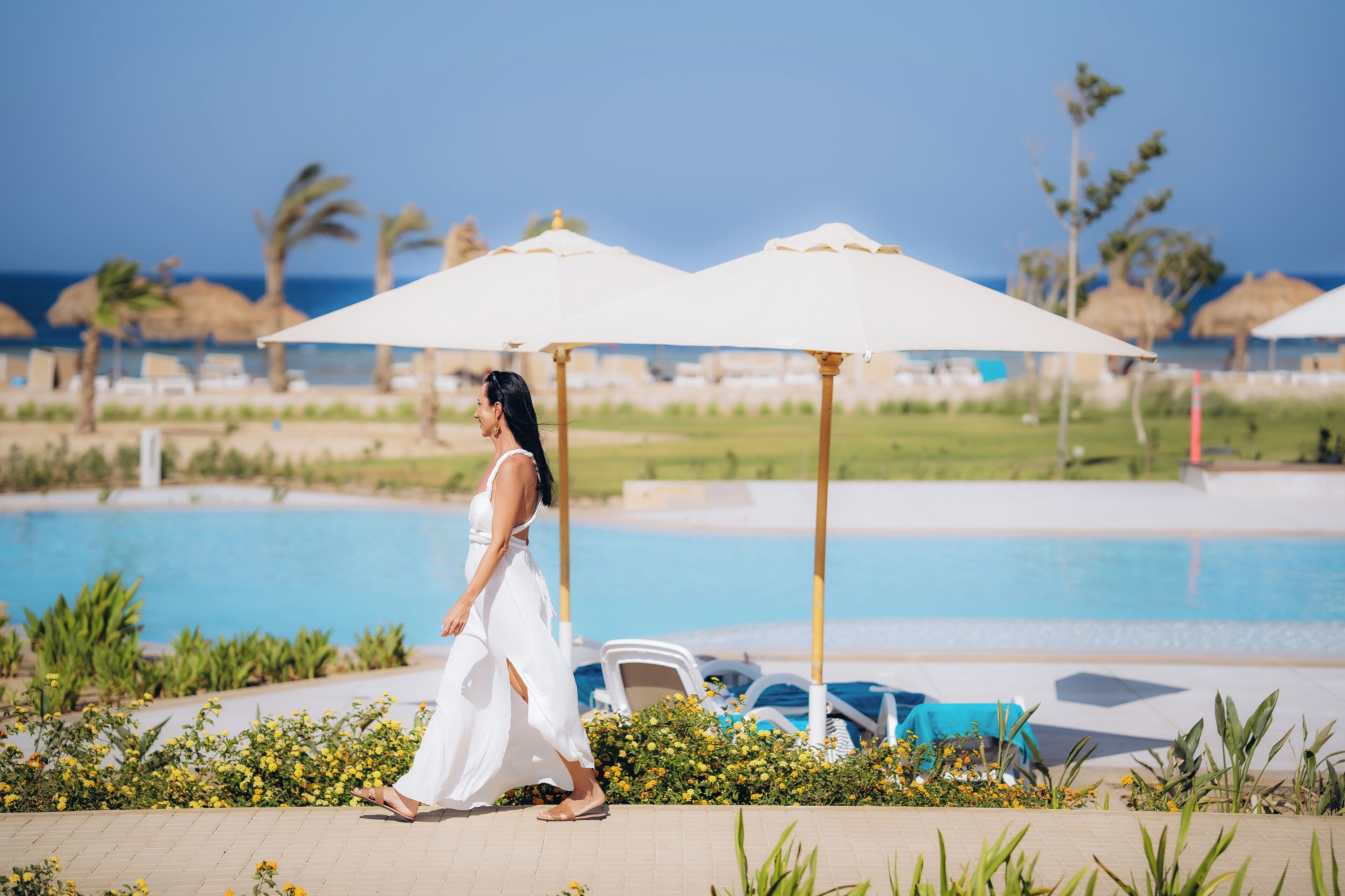 A poolside area with umbrellas, lounge chairs, and a clear view of the ocean.