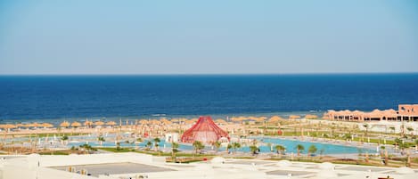 Un resort con diverse piscine, una grande struttura rossa e una spiaggia attrezzata con ombrelloni.