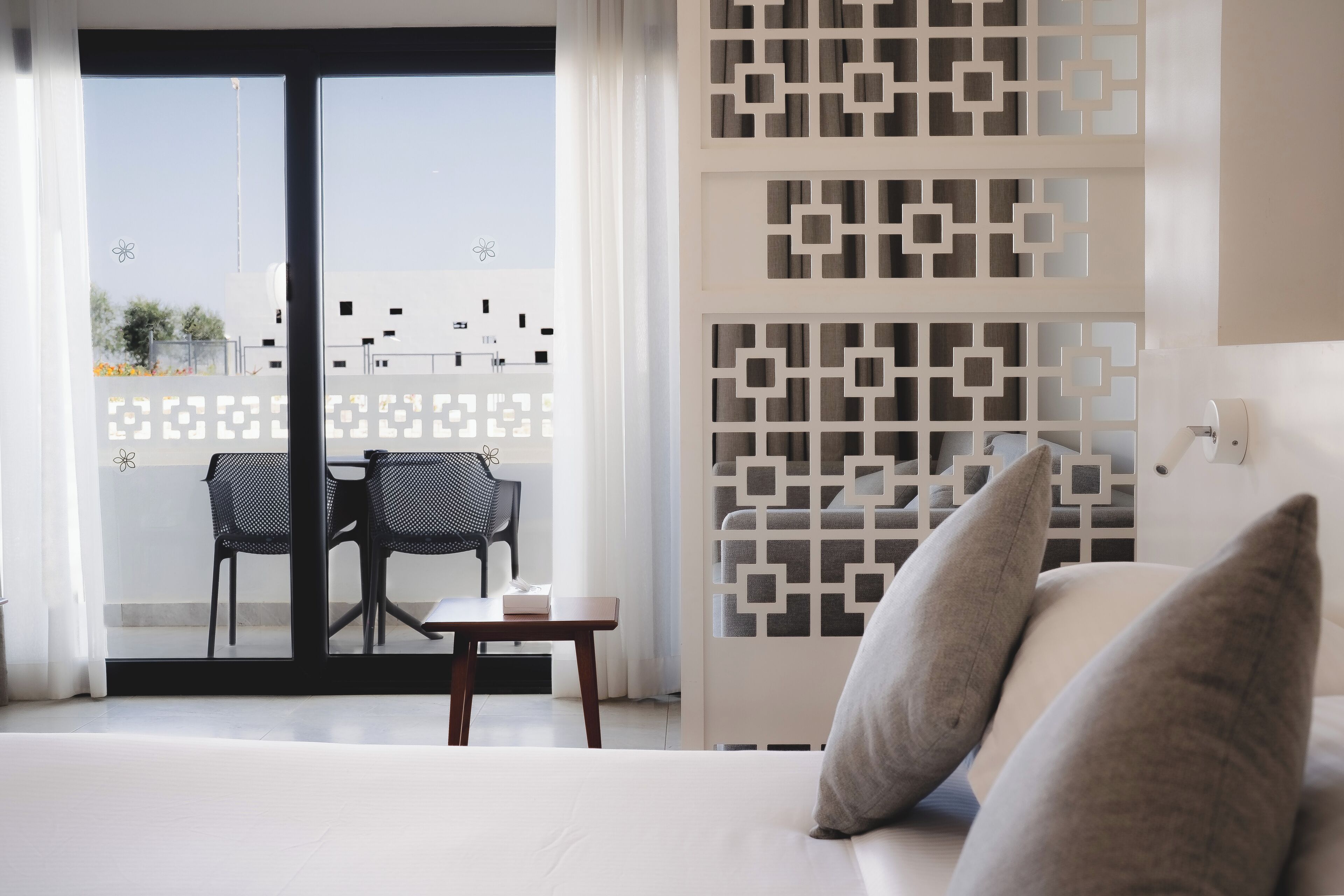 Een moderne hotelkamer met een balkon, een zithoek met twee stoelen en een tafel, en een decoratieve witte scheiding.