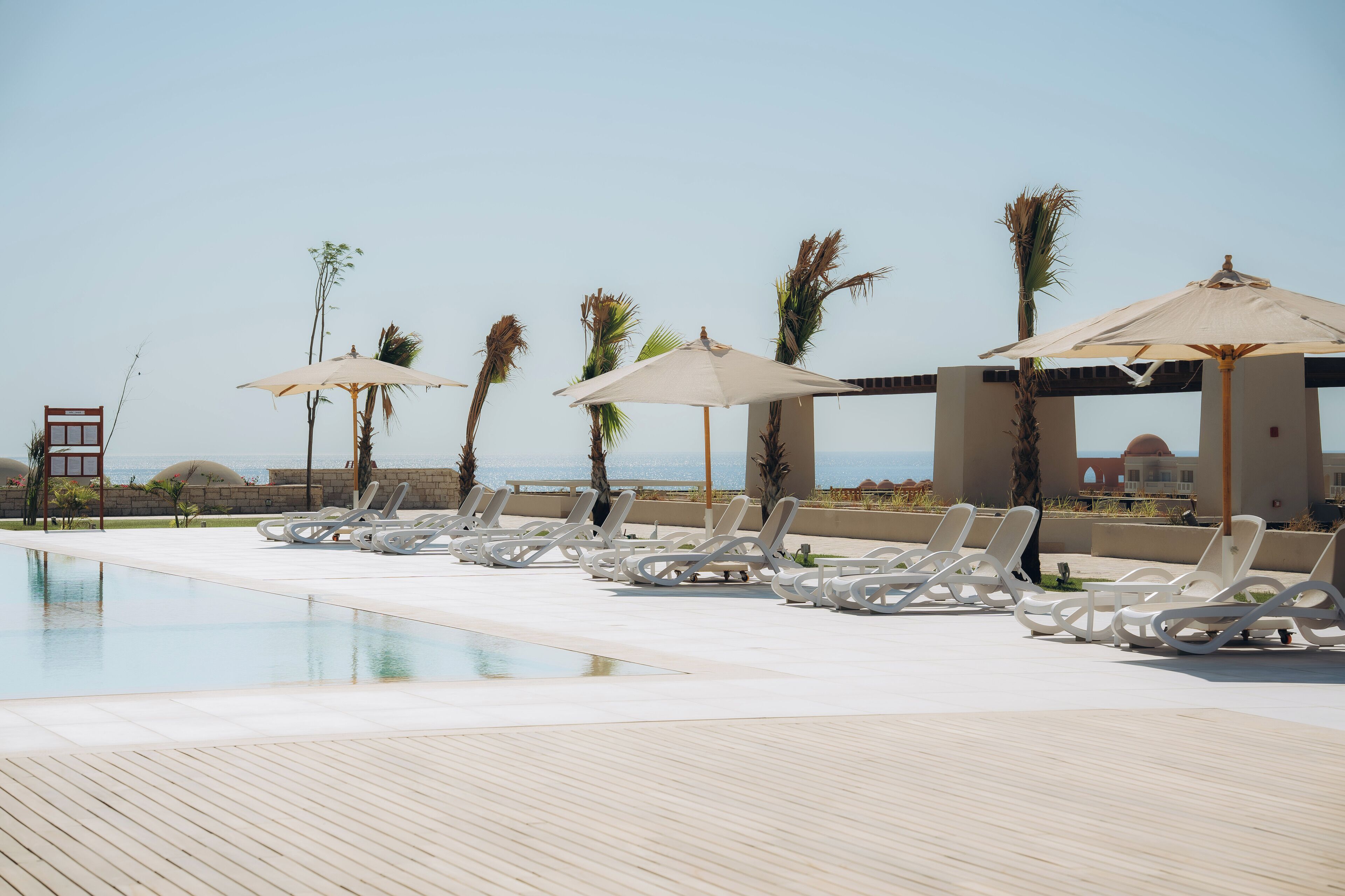 A poolside area with lounge chairs and umbrellas, a wooden deck, and a view of the ocean.