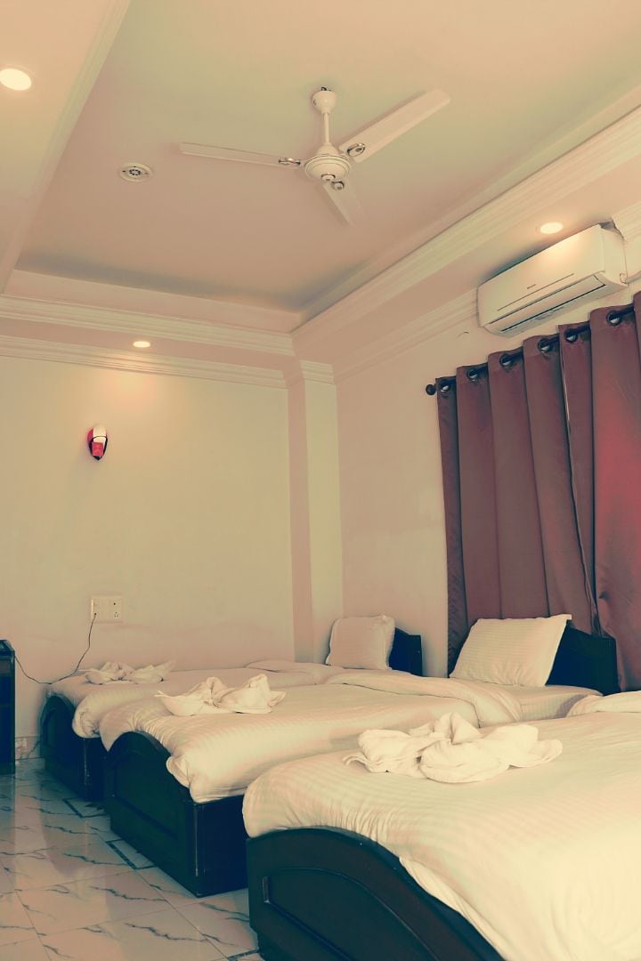 A hotel room with three beds, a ceiling fan, an air conditioning unit, and a wall-mounted fire alarm.