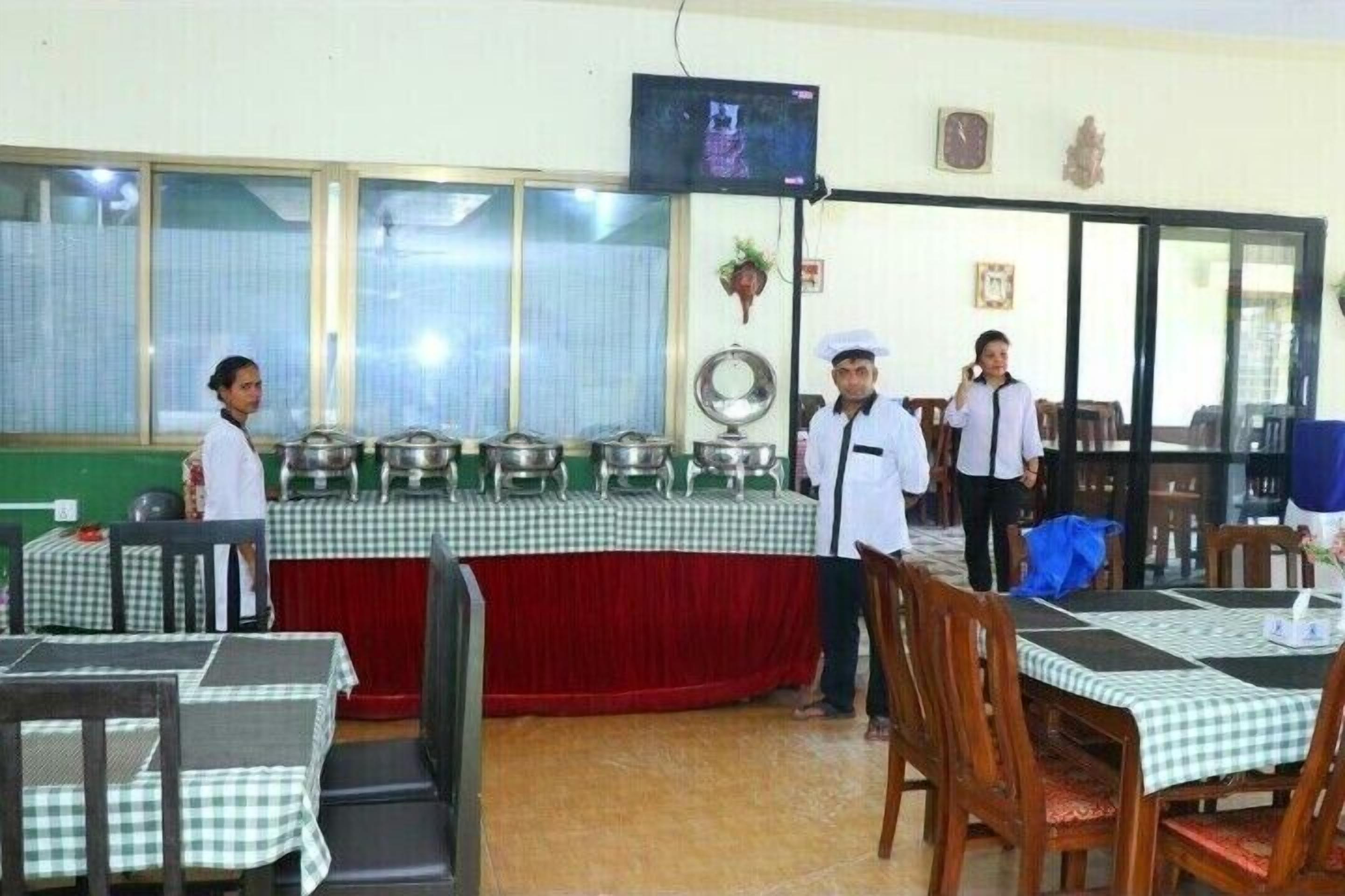 Un comedor con mesas cubiertas con manteles a cuadros, una barra de buffet con varios platos de comida, y un televisor colgado en la pared.