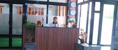 A reception desk with a clock, potted plants, and a sign indicating Nepal, China, and Thailand.