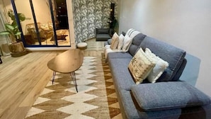 Un salon moderne avec un canapé gris, un tapis à motifs et une porte-fenêtre coulissante donnant sur un coin repas.