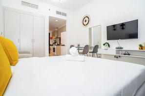 Ein Hotelzimmer mit einem Bett, einem Schreibtisch mit Flachbildfernseher, einer Essecke mit Stühlen und einer Küche im Hintergrund.