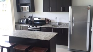A modern kitchen with a central island, dark cabinets, stainless steel appliances, and a microwave.