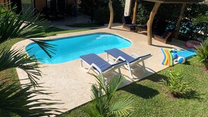 A swimming pool with lounge chairs, a small covered area, and inflatable toys.