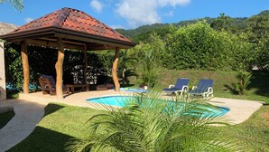 A covered outdoor area with a pool, lounge chairs, and a gazebo.