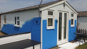 Et lille, etetages hus med blå og hvide facader, en fordør og en lille terasse med et bord og stole.