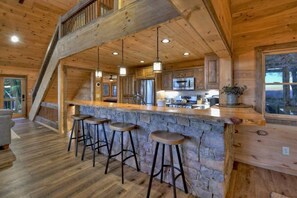 A wooden interior with a stone bar and stools, a kitchen area, and a staircase. - Altitude Blue Ridge - Awesome Views & 4 King Beds (Blue Ridge)