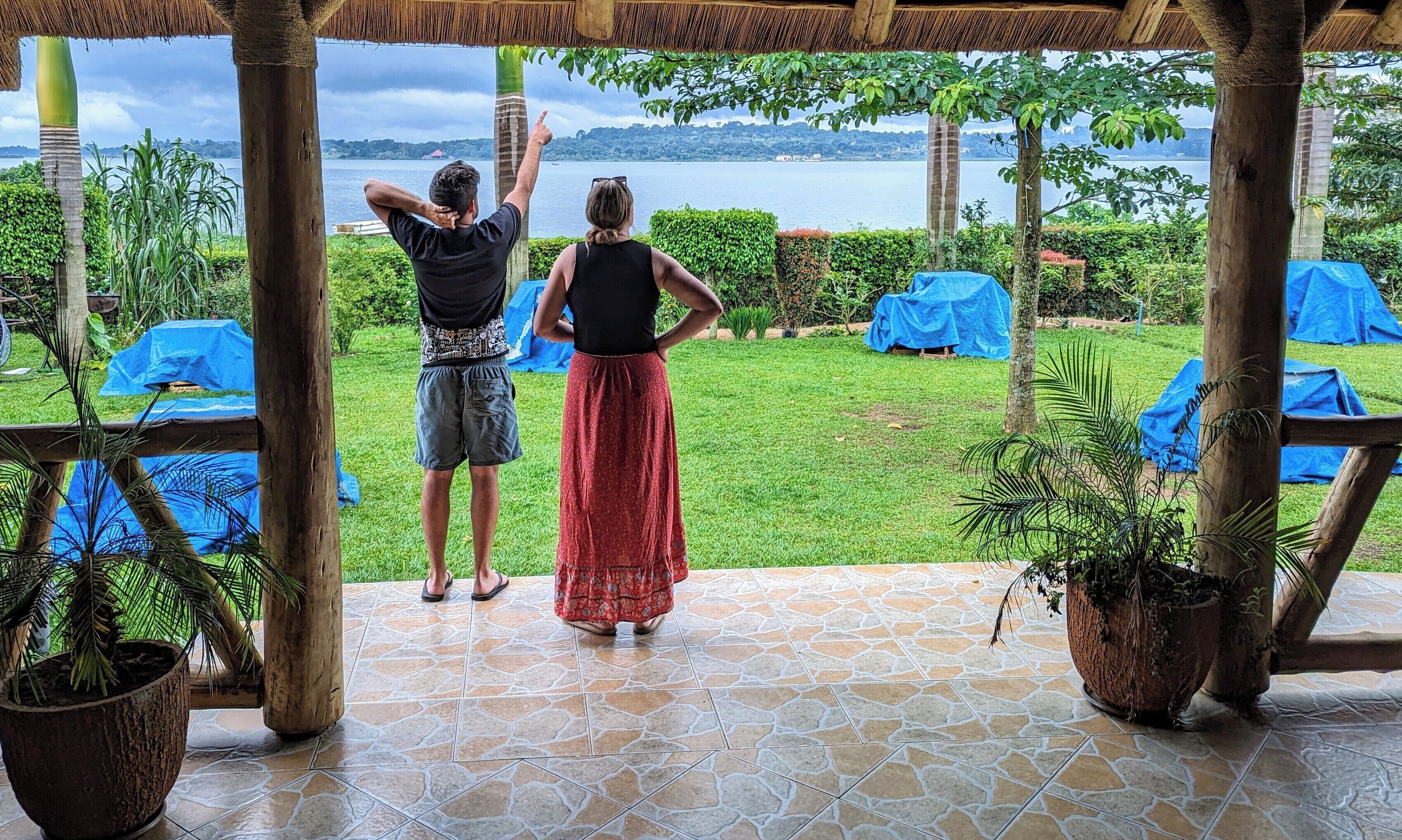 Un espacio al aire libre techado con vistas a un lago, techo de paja y suelo de baldosas.