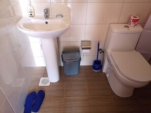 Un baño con lavamanos blanco, inodoro y un trapeador azul.