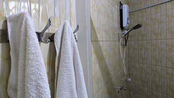 Un baño con toallas blancas colgadas en un perchero, una ducha con cabezal de ducha manual y un dispensador de jabón de pared.