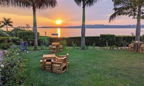 Un jardín con muebles de madera y vistas al atardecer sobre un cuerpo de agua.