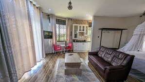 Un salon avec un canapé en cuir, une table basse et un téléviseur. Il y a également un coin cuisine avec des placards et une table à manger avec des chaises.