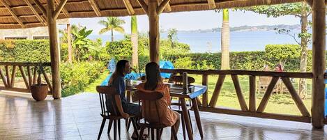 Un espacio de estar al aire libre con techo y vistas al mar, mobiliario de madera y plantas en macetas.