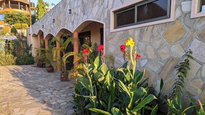 Un bâtiment en pierre doté d’une cour, de plantes en pot et d’une structure surmontée d’un toit de chaume.