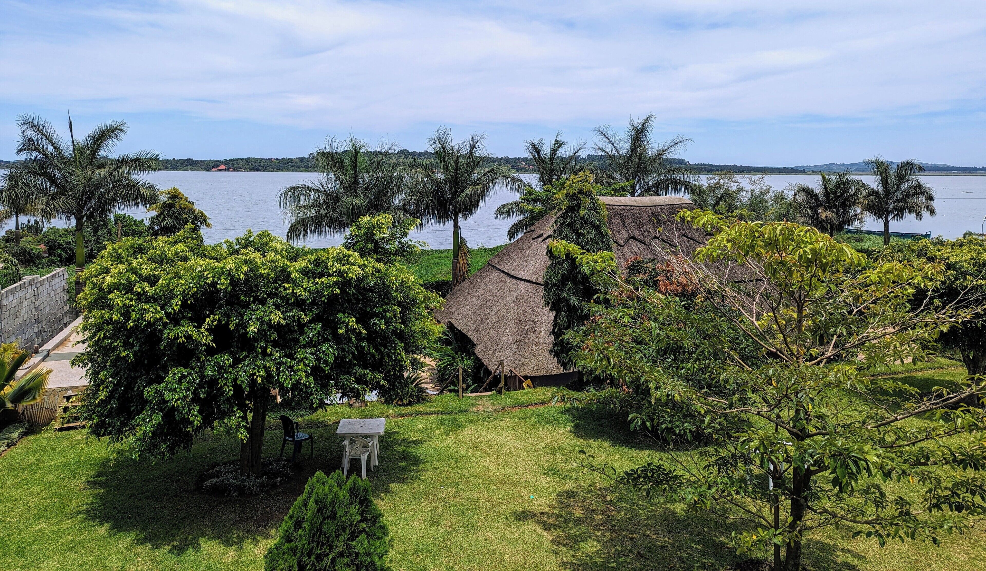 A thatched-roof house surrounded by lush greenery and a body of water.