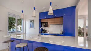 A modern kitchen with blue cabinets, white countertops, and three bar stools. - Modern 8-guest house with garden & BBQ (La Baule-Escoublac)