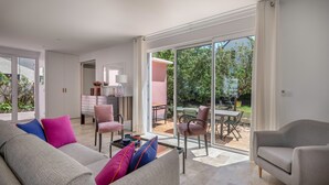 A modern living room with a grey sofa, a grey armchair, and a pink chair. There is a dining table with chairs outside a glass door. - Modern 8-guest house with garden & BBQ (La Baule-Escoublac)