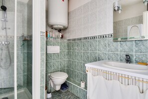 Uma casa de banho com chuveiro, sanita, lavatório e porta-toalhas.