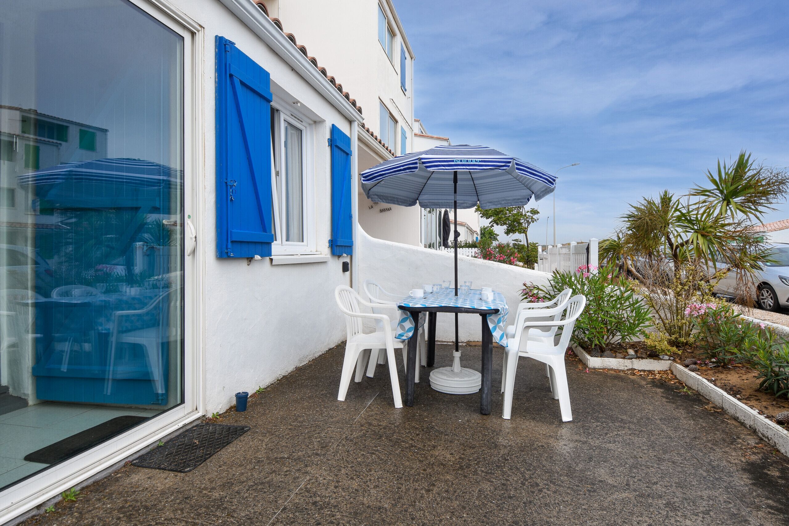 A patio with a table and chairs, an umbrella, and a white building with blue shutters.