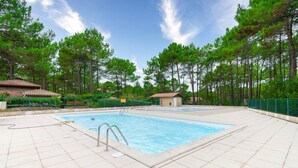 A swimming pool with a tiled deck, surrounded by trees and a small building. - House for 4 with pool in Lacanau (Lacanau)