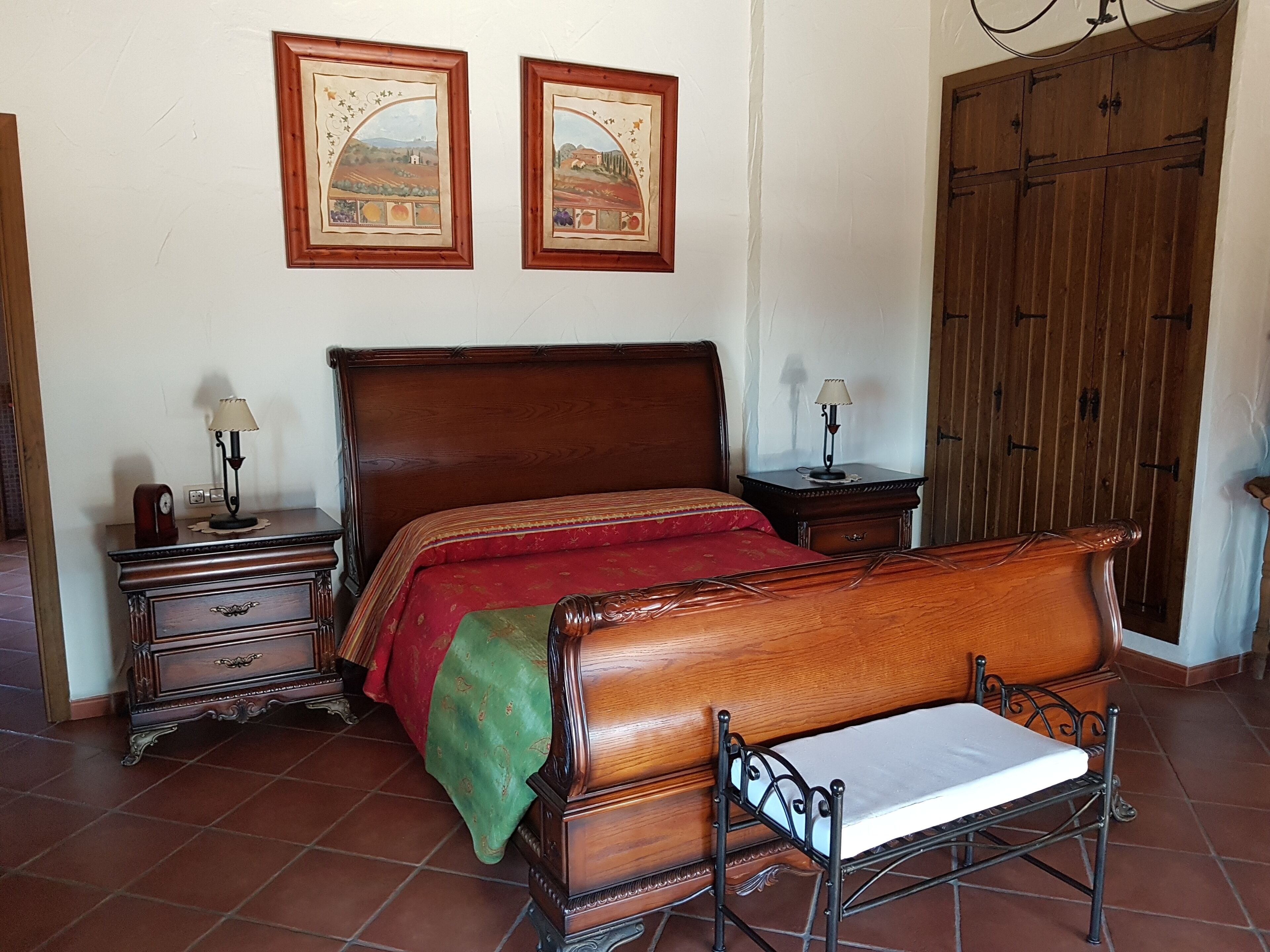 Een slaapkamer met een houten bed, een nachtkastje, een dressoir en twee wandlampen.