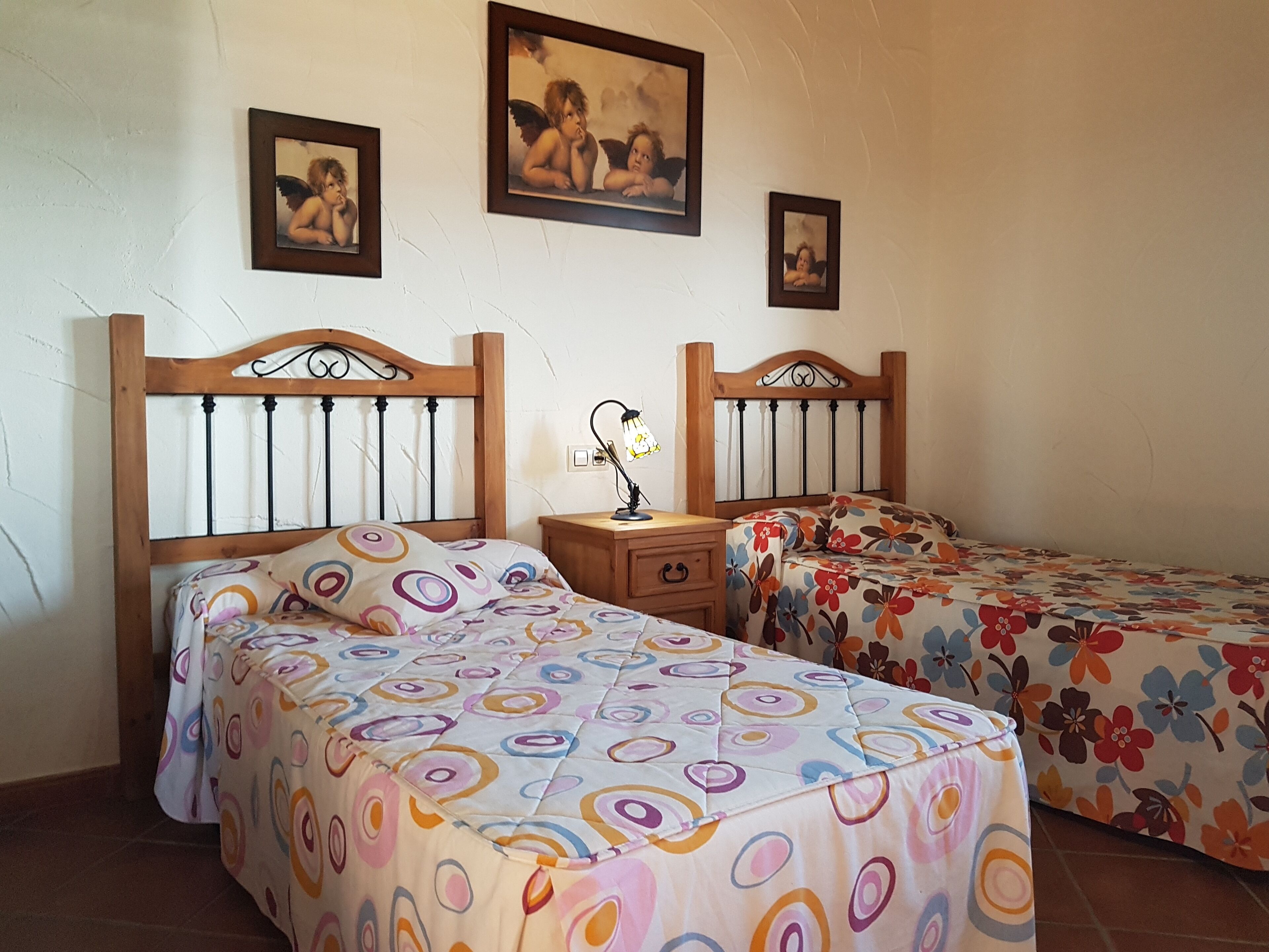A room with two wooden beds with circular-patterned bedding, a nightstand with a lamp, and three framed pictures on the wall.