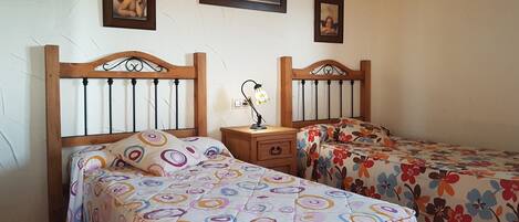A room with two wooden beds with circular-patterned bedding, a nightstand with a lamp, and three framed pictures on the wall.