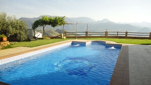 A rectangular swimming pool with a tiled edge, surrounded by a wooden fence and a grassy area.